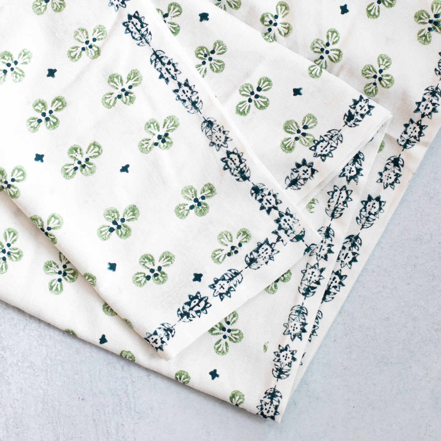 Folded hand blocked tablecloth with evergreen and midnight blue dogwood floral on a gray background