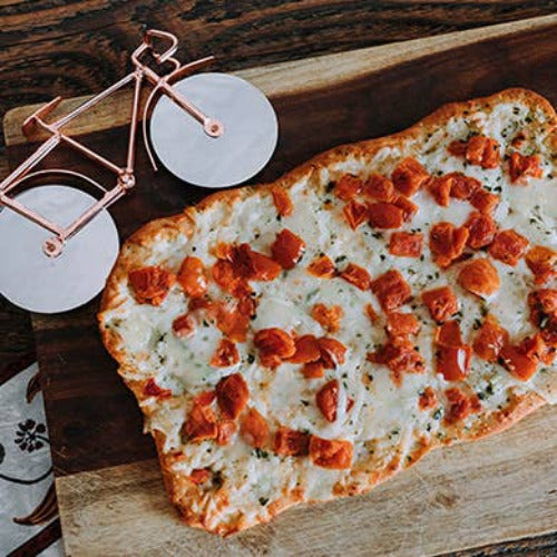 Flatbread pizza with pepperoni on a wooden board with bicycle shaped pizza cutter in the background
