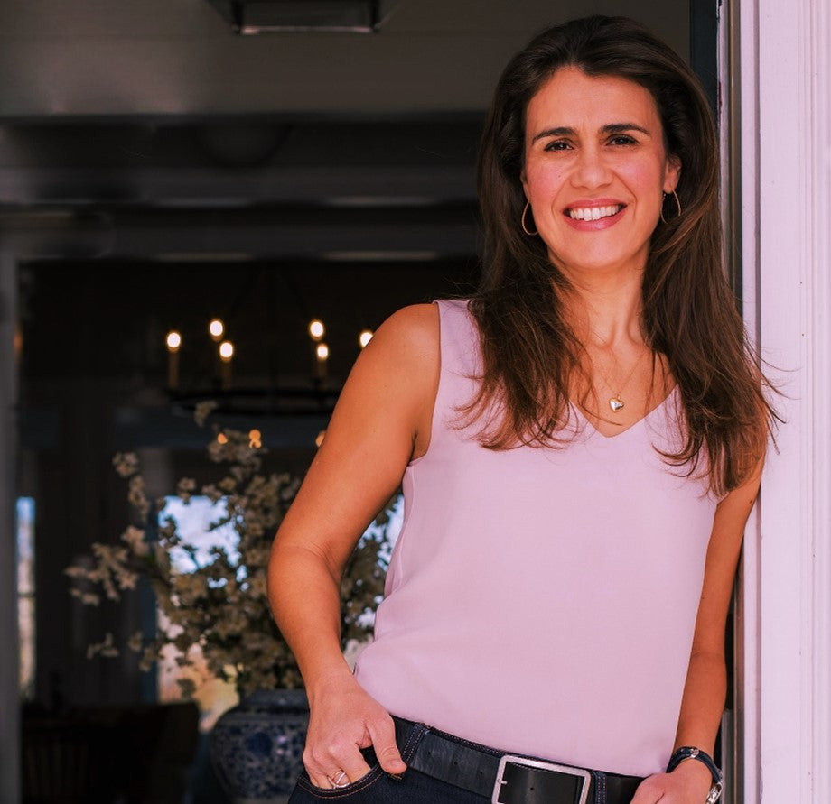 woman wearing blue jeans and a pink sleeveless v-neck top leaning on open door frame with her hands in her pocket