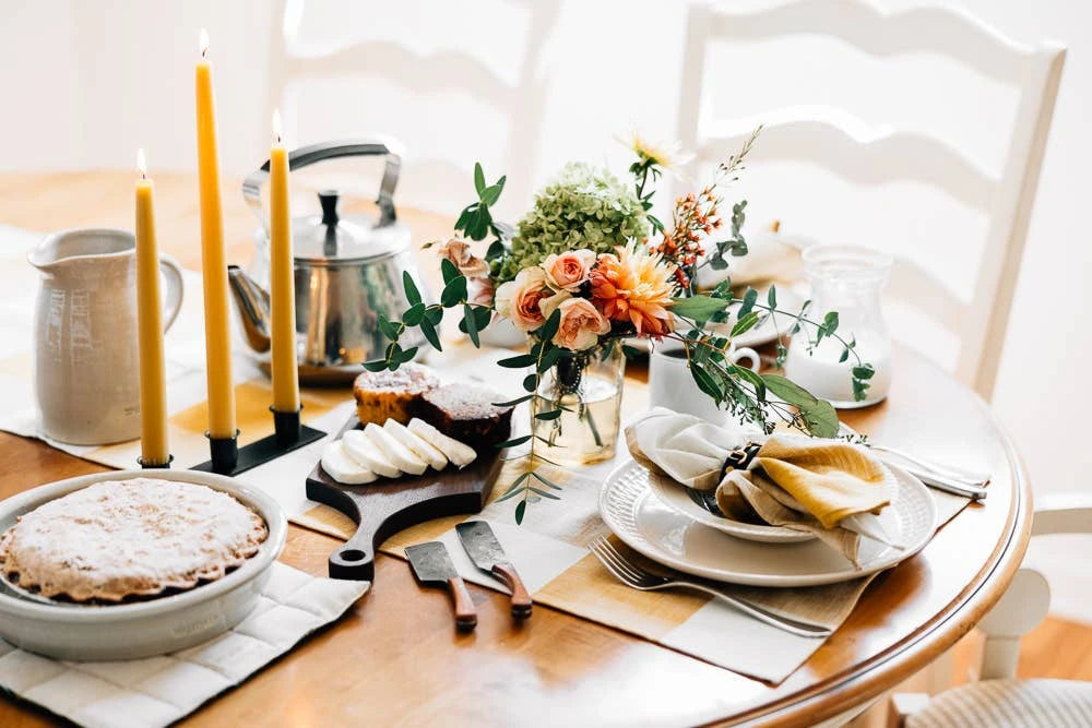 Image of a table setting. Table is set with candles, a pie, some roses and a tea pot