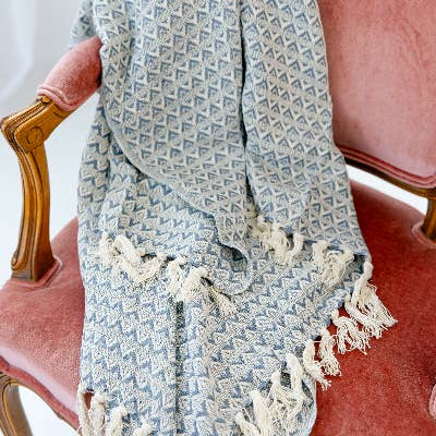 A soft blue handwoven throw is overlayed on a pink victorian accent chair