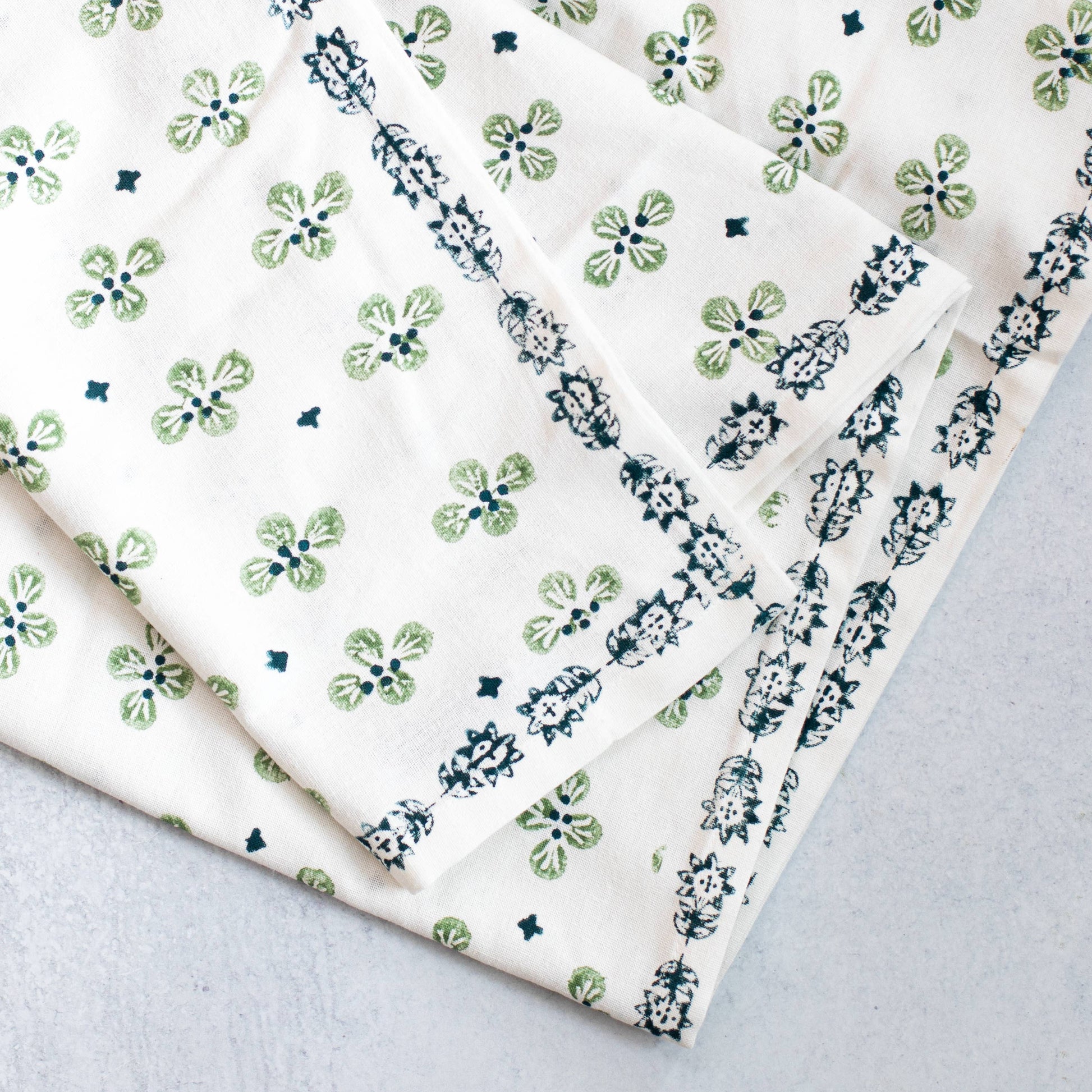 Folded hand blocked tablecloth with evergreen and midnight blue dogwood floral on a gray background
