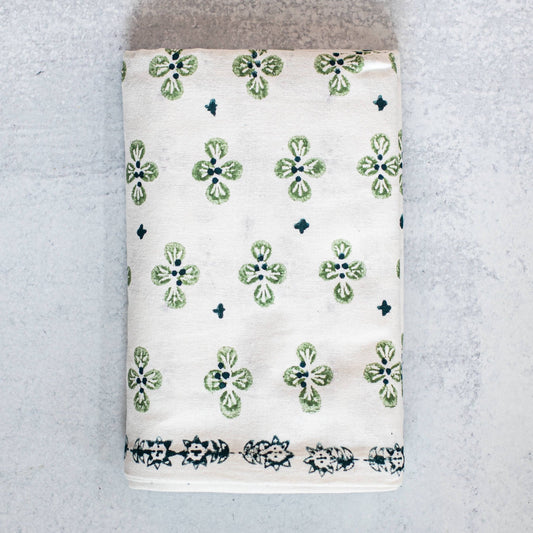 Folded hand blocked tablecloth with evergreen and midnight blue dogwood floral on a gray background