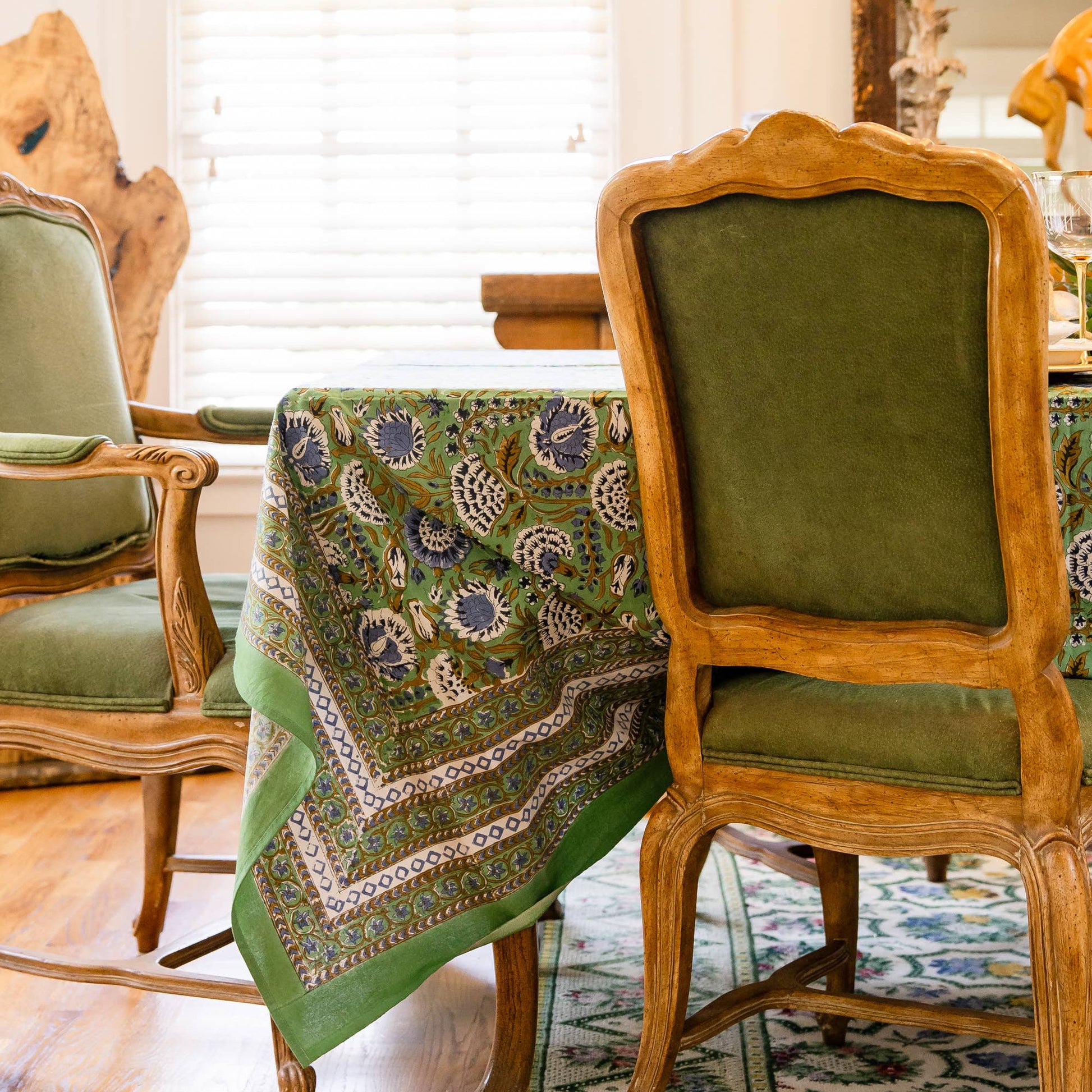 Green floral motif patterned hand blocked tablecloth draped over a table in a italian inspired room with a mirror and window blinds