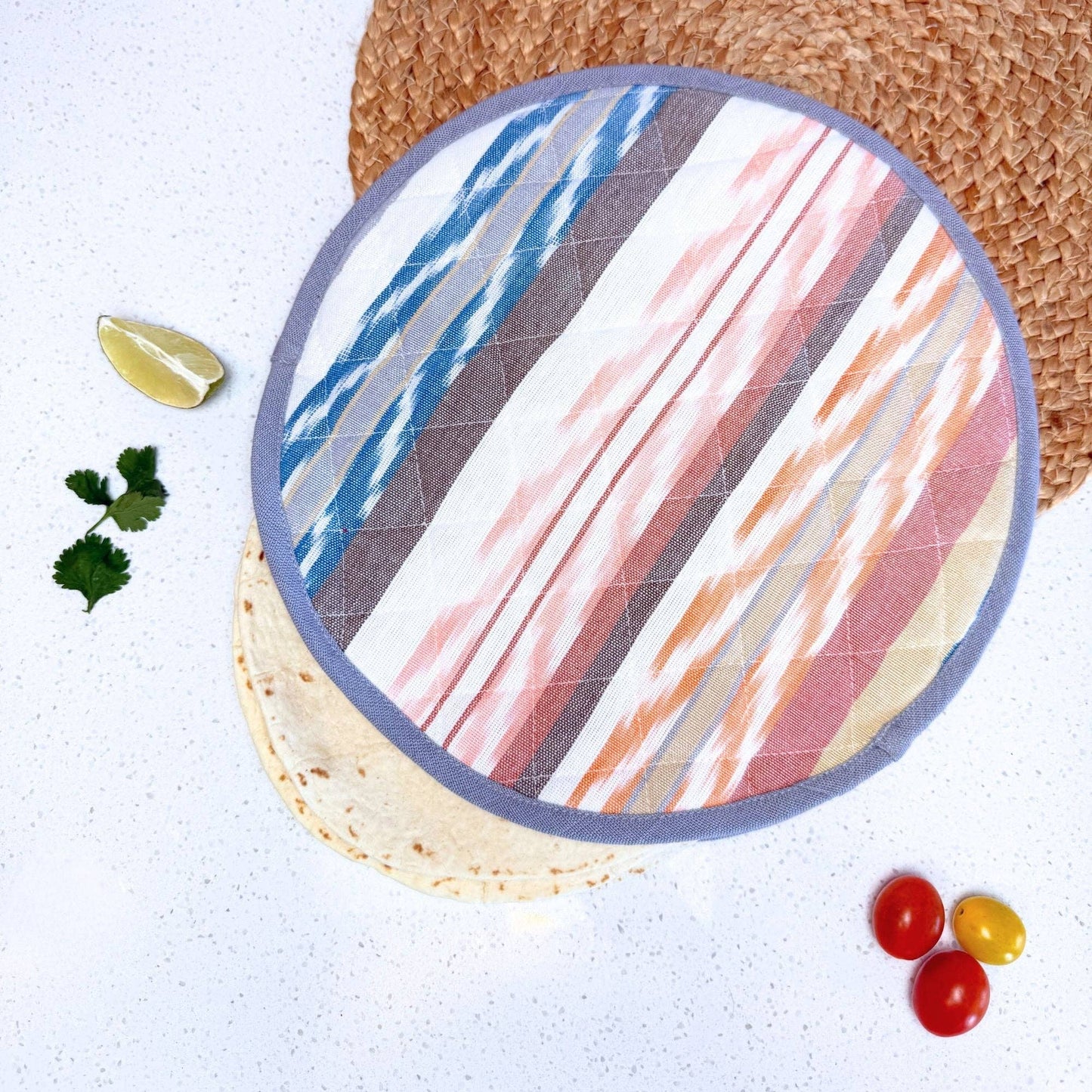 Round colorful tortilla warmer with a tortilla, lemon, and vegetables on a white kitchen counter