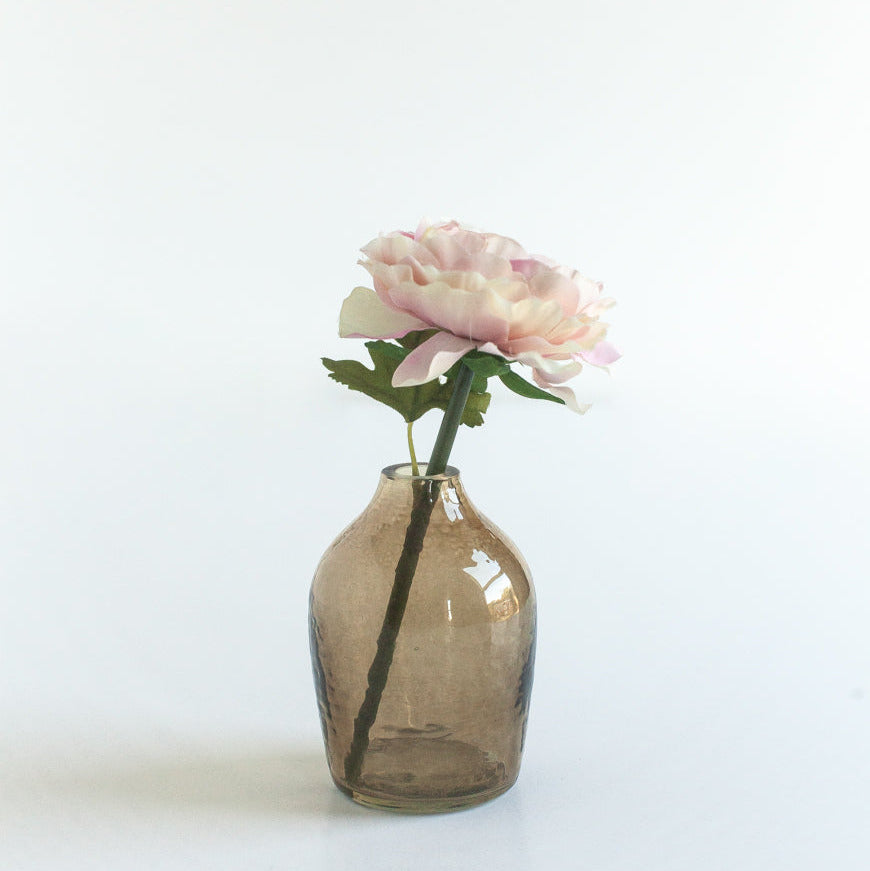 Small smoke / brown glass bud vase with a single pink flower on a white background