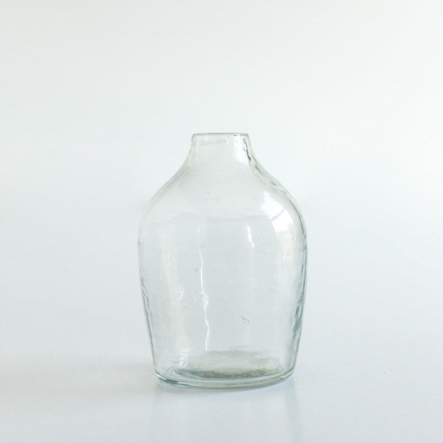 Clear handblown hammered glass bud vase on a white background