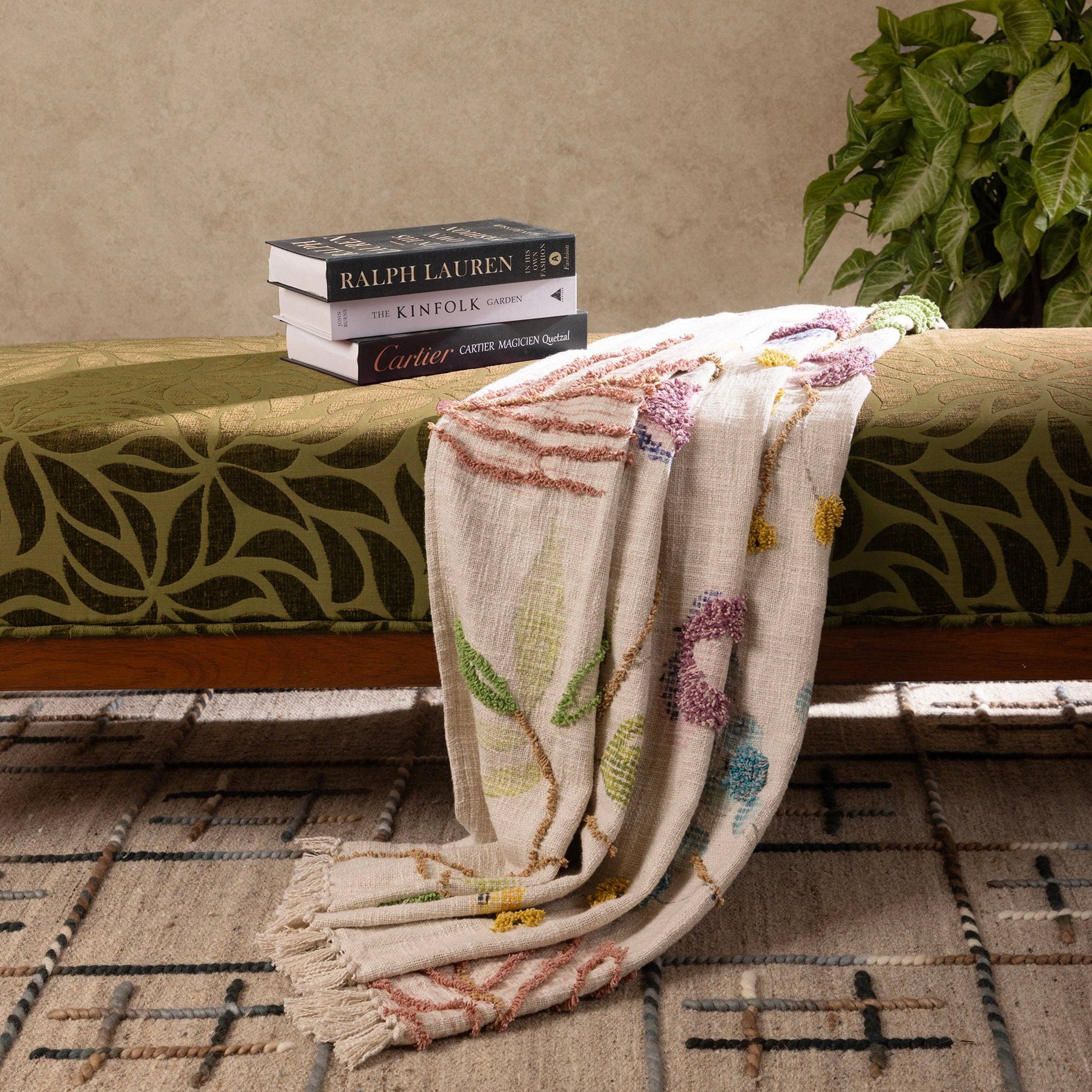 handcrafted decorative throw blanket with floral patterns draped over a wooden bench against a beige wall.