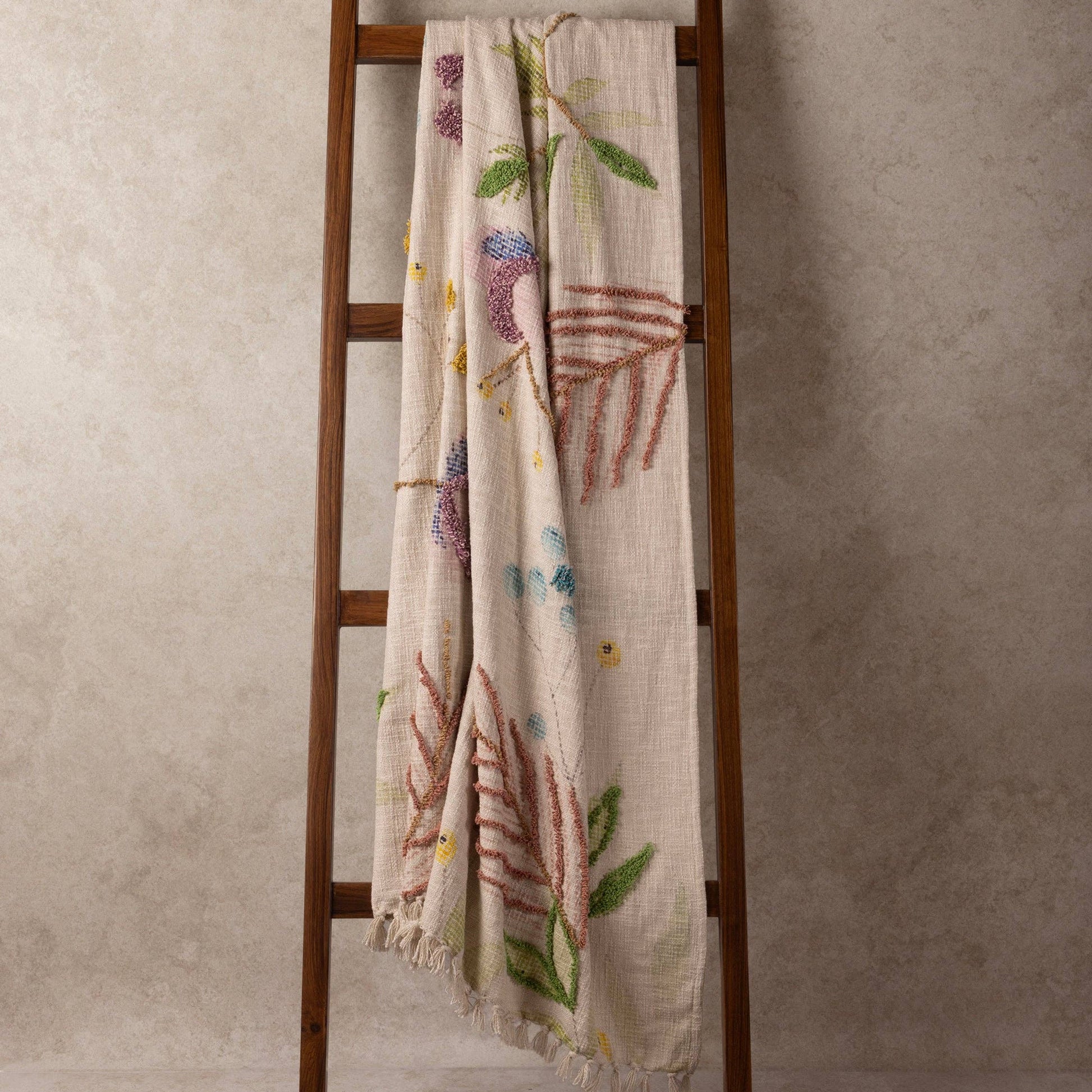 Decorative ladder with a handcrafted floral-patterned blanket against a neutral wall.