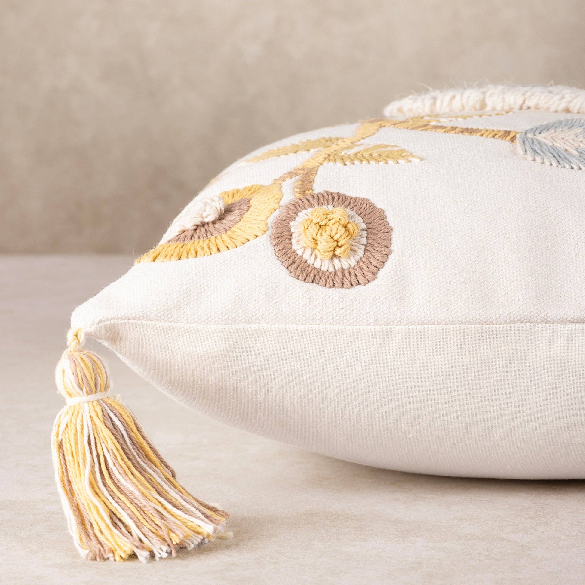handmade decorative pillow with embroidery and tassel on a neutral background