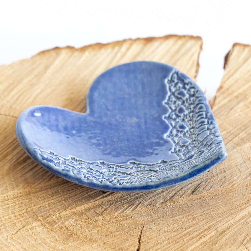 Blue handmade ceramic heart on a wooden log with a white background