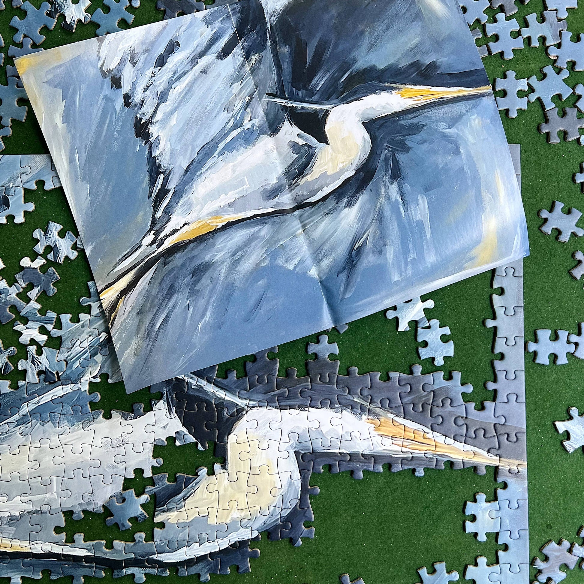 Jigsaw puzzle with a completed section featuring a blue heron painting on a green surface.