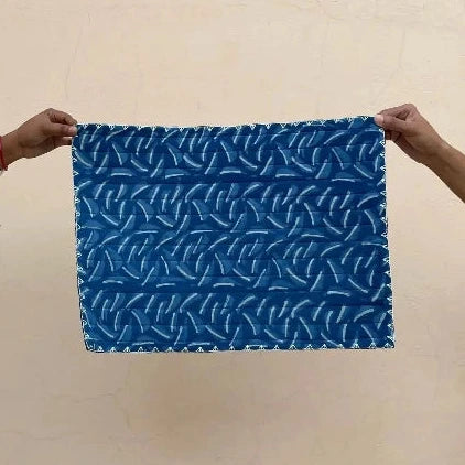 Blue quilted placemat with white pattern held by two hands against a beige background