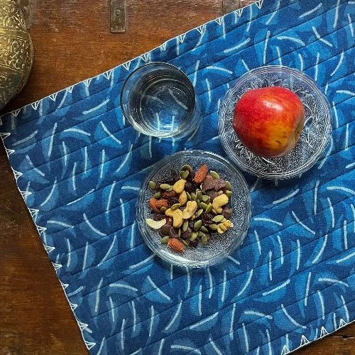 Two small glass bowls with dried fruits and a red apple on a blue patterned placemat.
