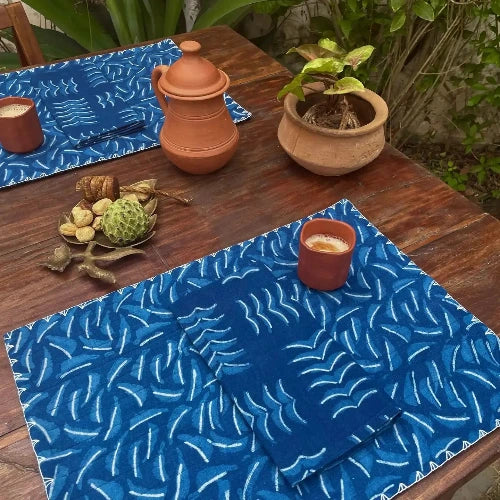 Blue patterned placemats on a wooden table with cups and a pot.