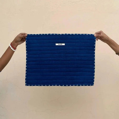Blue quilted plaacemat held by two hands against a beige background