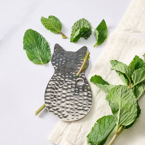 Cat-shaped stainless steel herb stripper with mint leaves on a white background