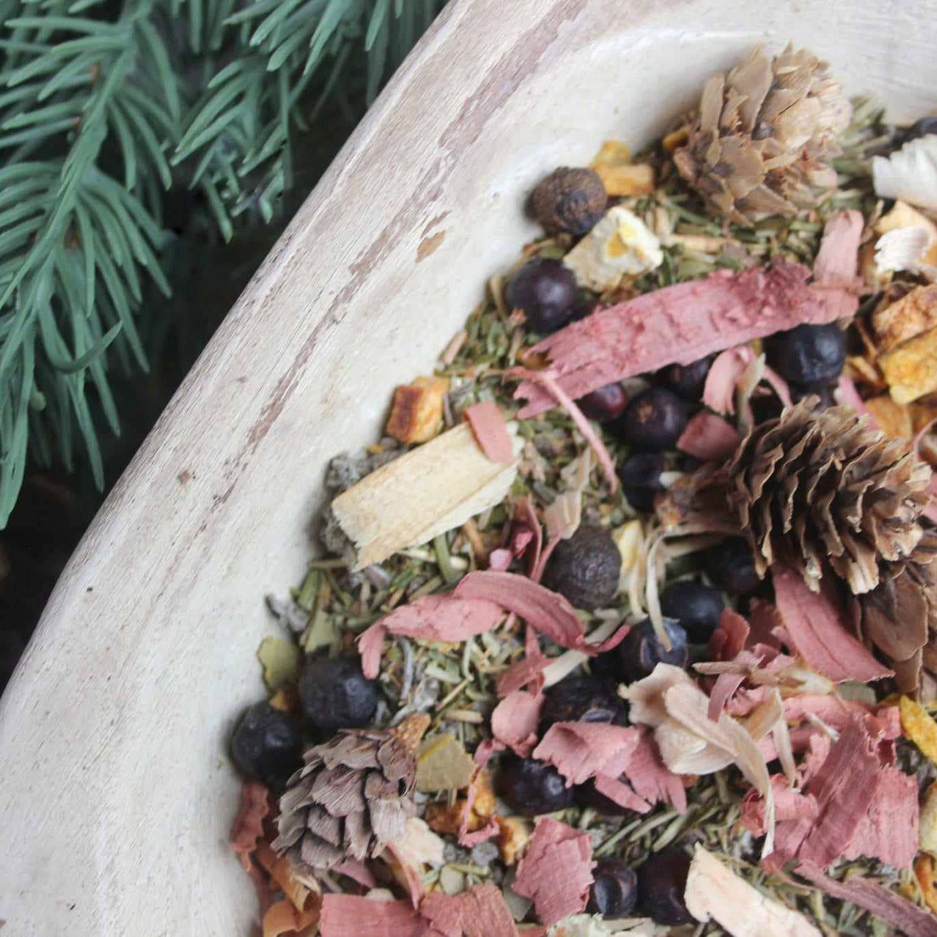 Holiday pop simmer mix with pine cones and berries in a white dish.