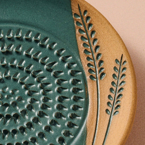 Close-up of a ceramic grater with textured design and leaf pattern on a pink background