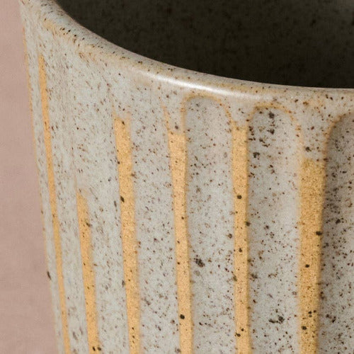 Close-up of a ceramic vase with textured surface and gold stripes on a pink background