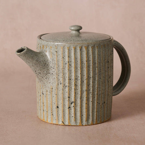 Ceramic teapot with ribbed design on a beige background