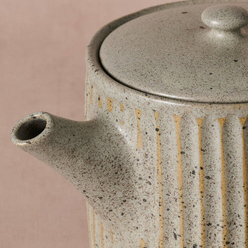 Close-up of a speckled handmade gray ceramic teapot on a pink background