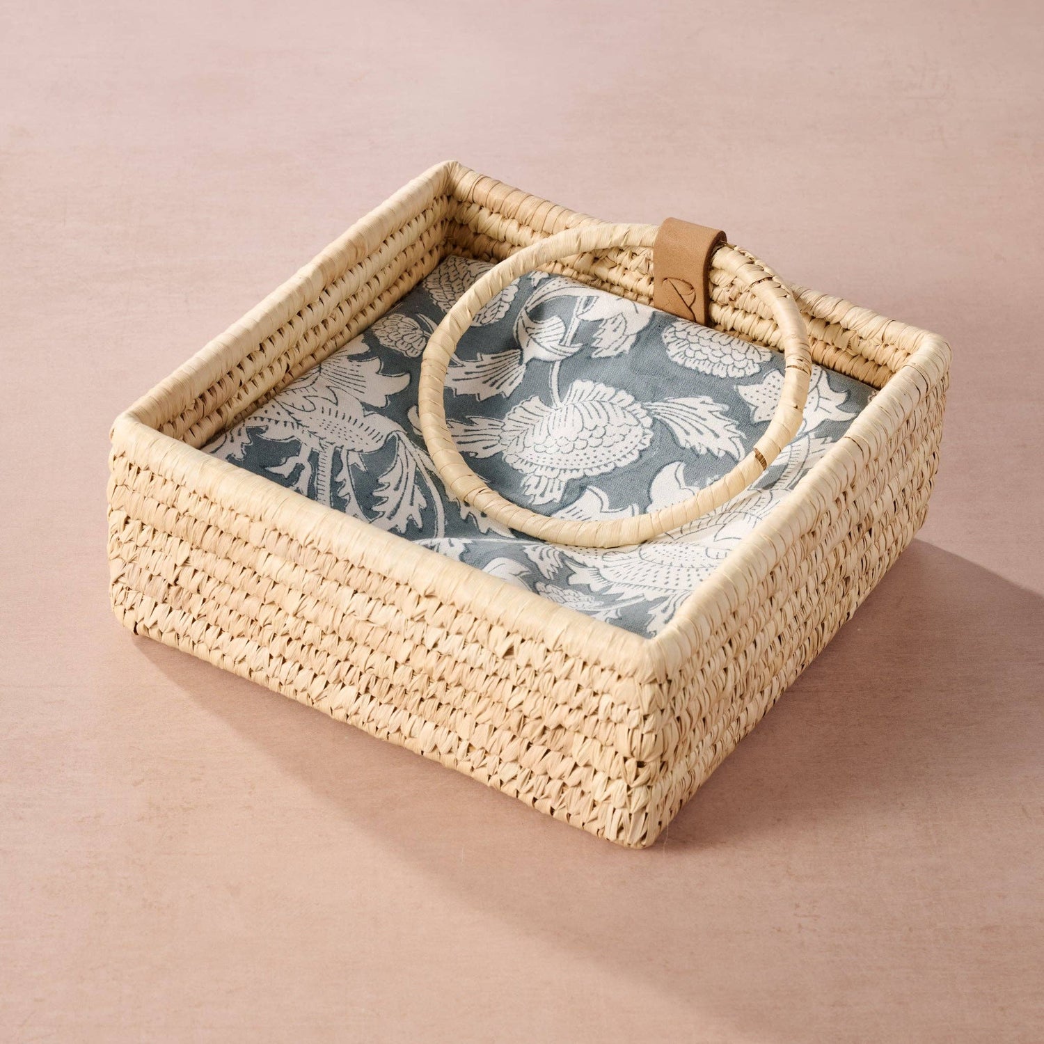 Hand woven napkin  holder with floral napkins on a pink background