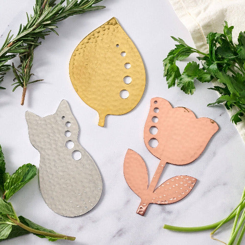 herb strippers in flower shape, cat shape and leaf shape on a marble surface with herbs