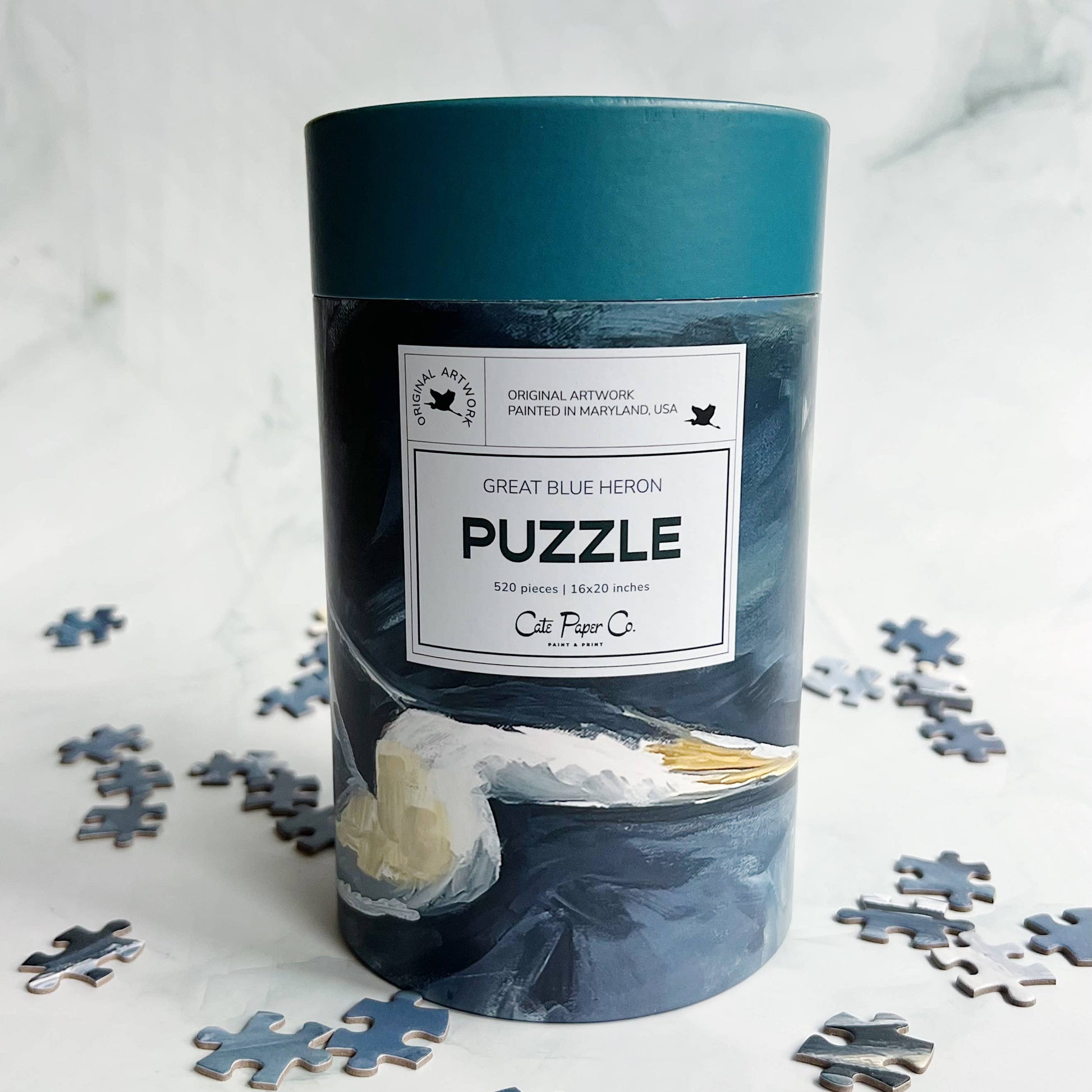 Blue Heron puzzle packaging with puzzle pieces on a light background