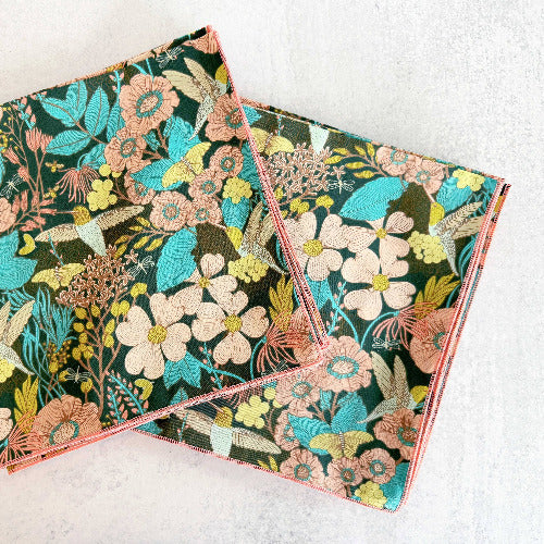 Two floral hummingbird-patterned cocktail napkins on a white surface