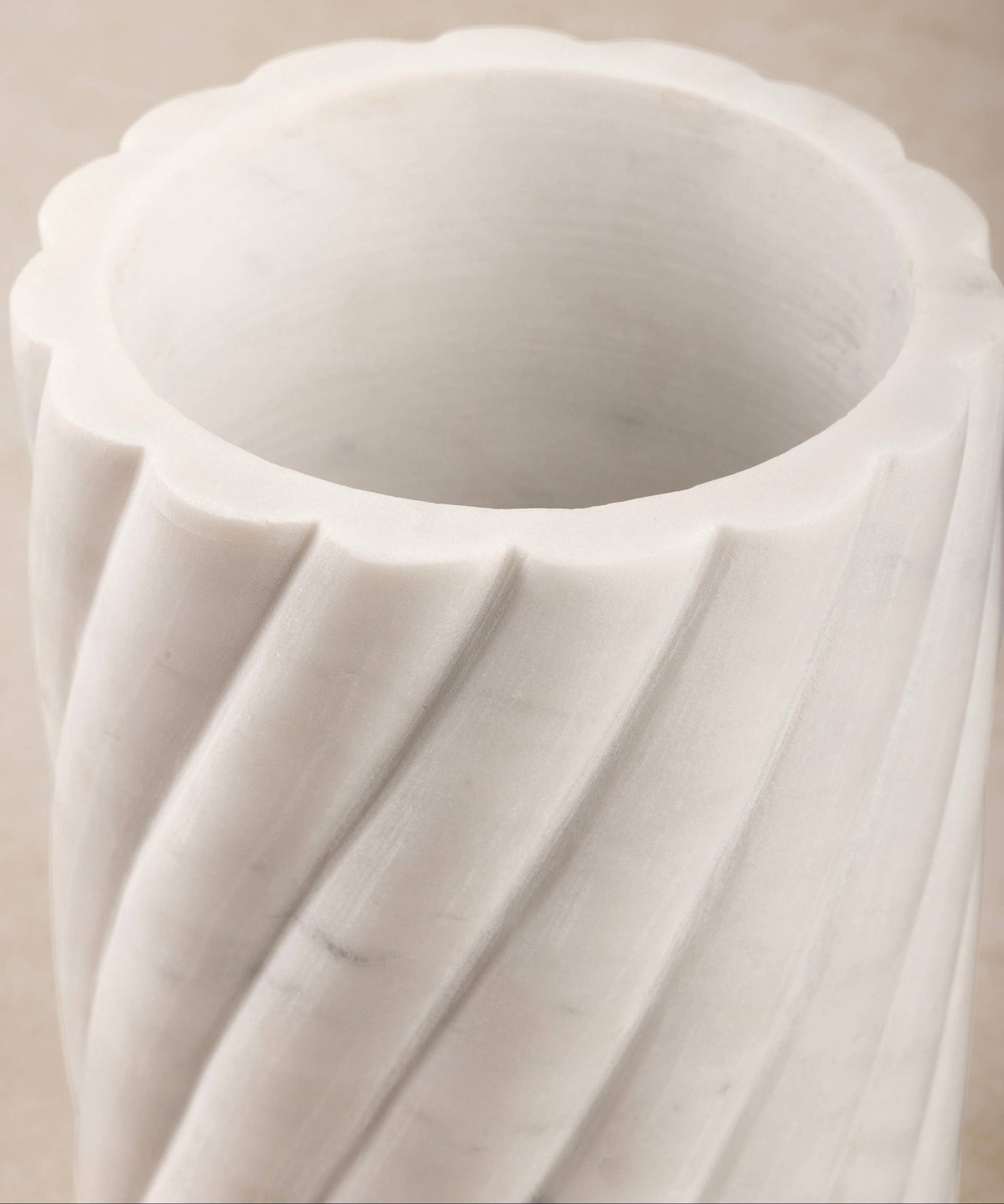 Close-up of a white marble vase or wine cooler with intricate ribbed design on a beige background