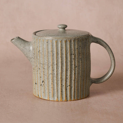 Ceramic teapot with ribbed design on a pink background