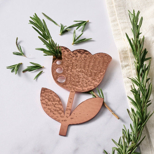 copper herb stripper in flower shape with rosemary leaves on a light background