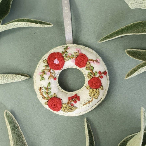 a wreathe felt ornament with Damascus red rose embroidery laying on a green background