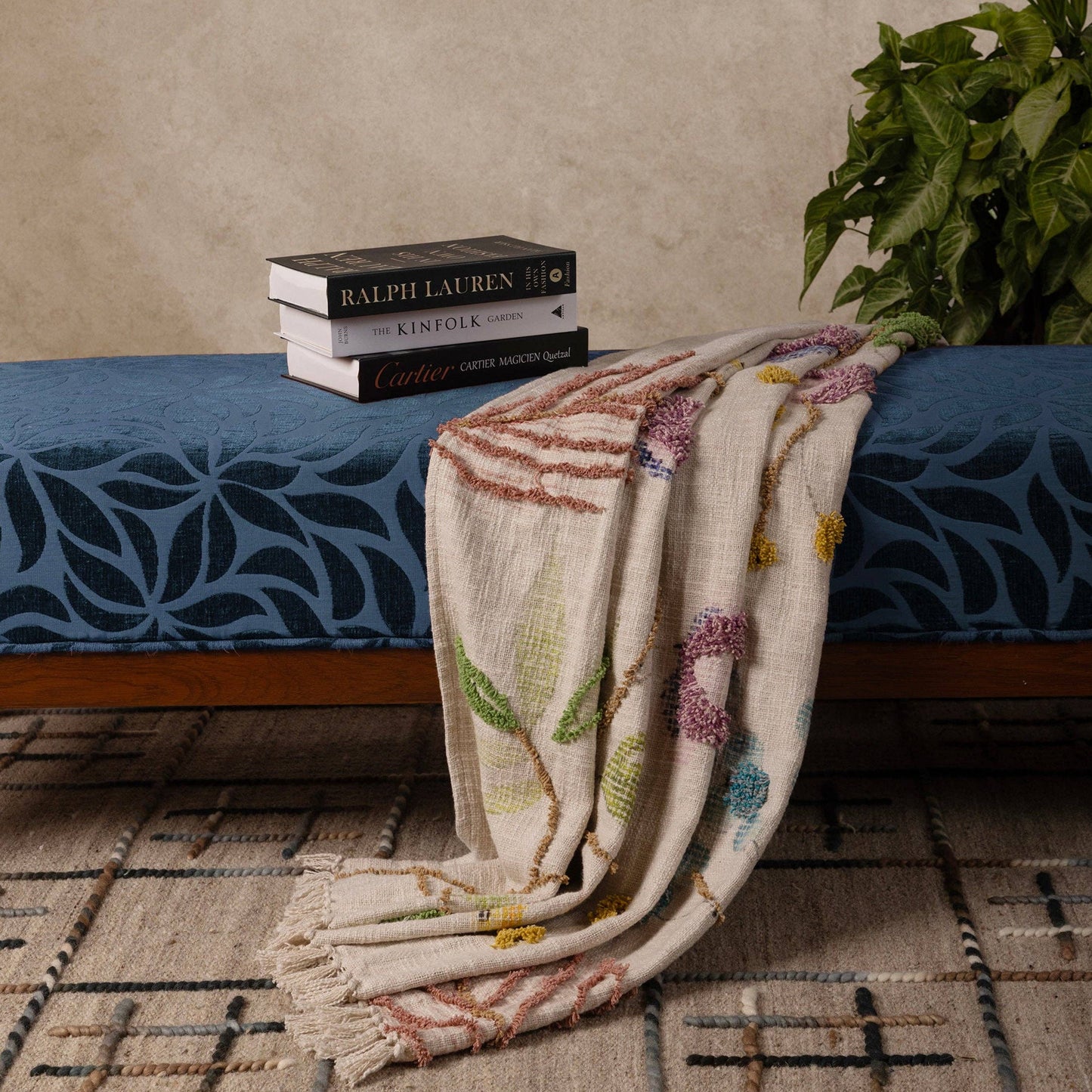 Decorative handcrafted throw blanket on a bed with books and a plant in the background