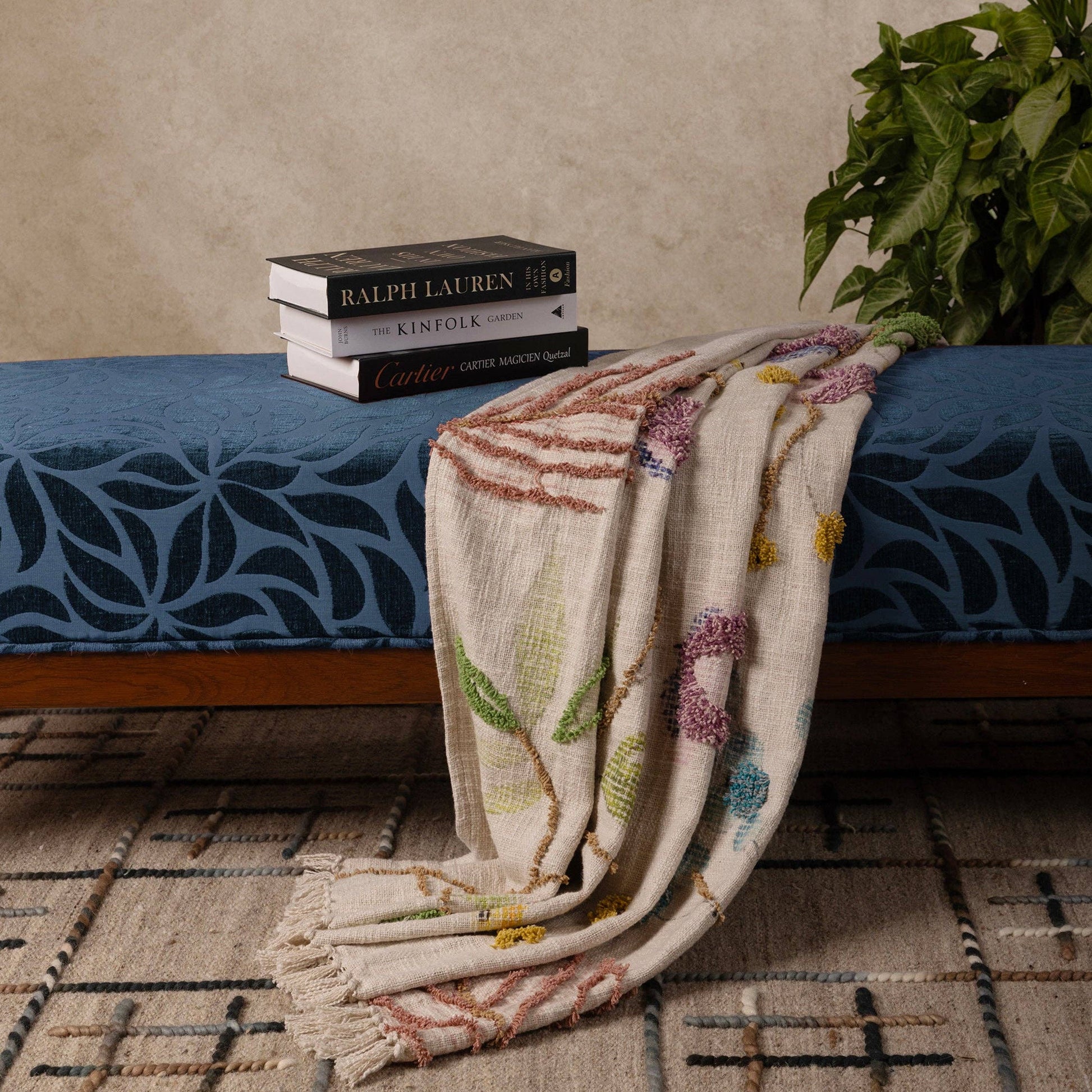 Decorative handcrafted throw blanket on a bed with books and a plant in the background